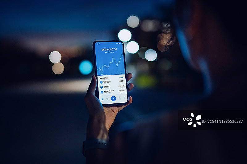 年轻女性在城市中使用手机App管理网上银行的肩部视角图片素材