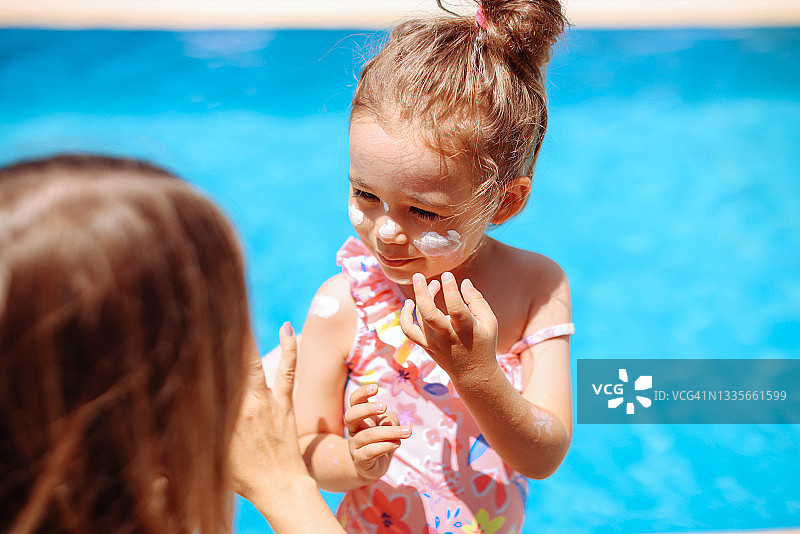 母亲在海滩上为小女儿涂抹防晒霜图片素材