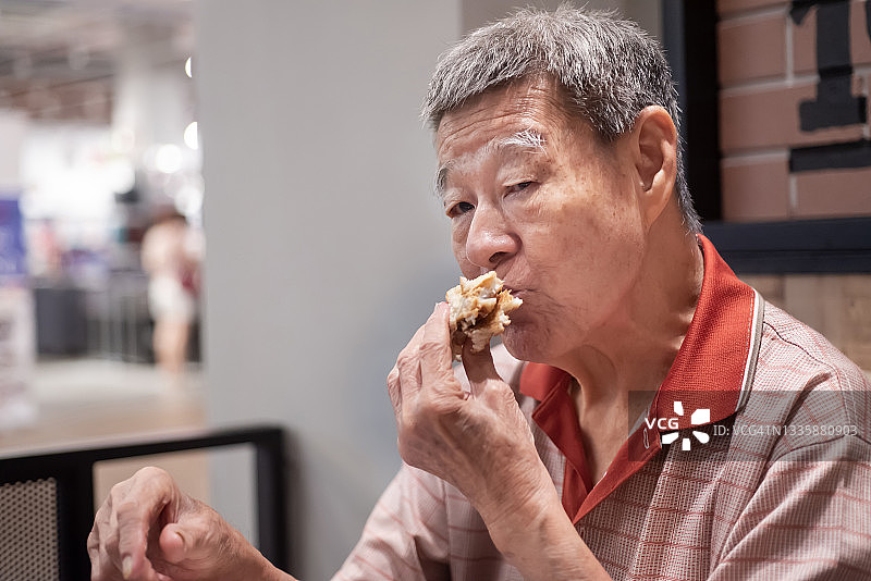 亚洲老人在快餐店享用美味汉堡图片素材
