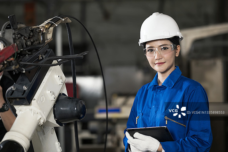 制造业的关键：女工业工程师手持数字平板电脑在汽车零部件生产线上工作，周围是机器人焊接机。她擅长生产过程改进和质量。图片素材
