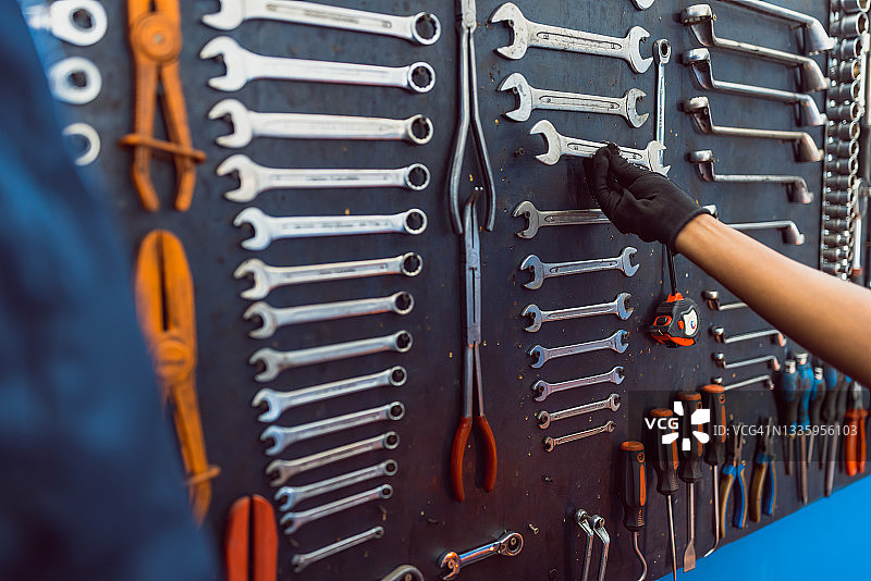 黑人女人从装有不同工具的黑色墙壁上取扳手图片素材
