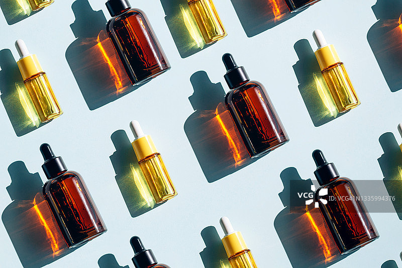 淡蓝色背景上的黄色琥珀色玻璃瓶液体，用于皮肤护理的精油或精华液，健康水疗概念图案图片素材
