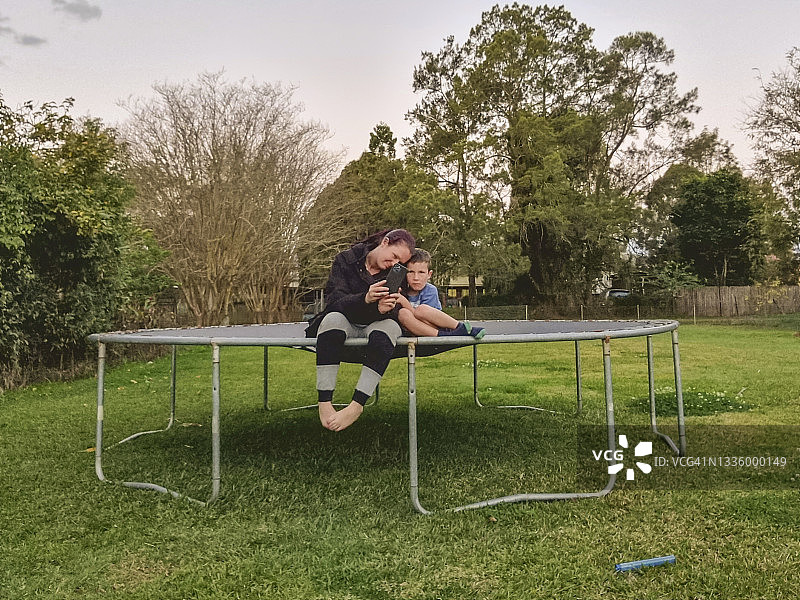 母子在蹦床上一起用手机拍照图片素材