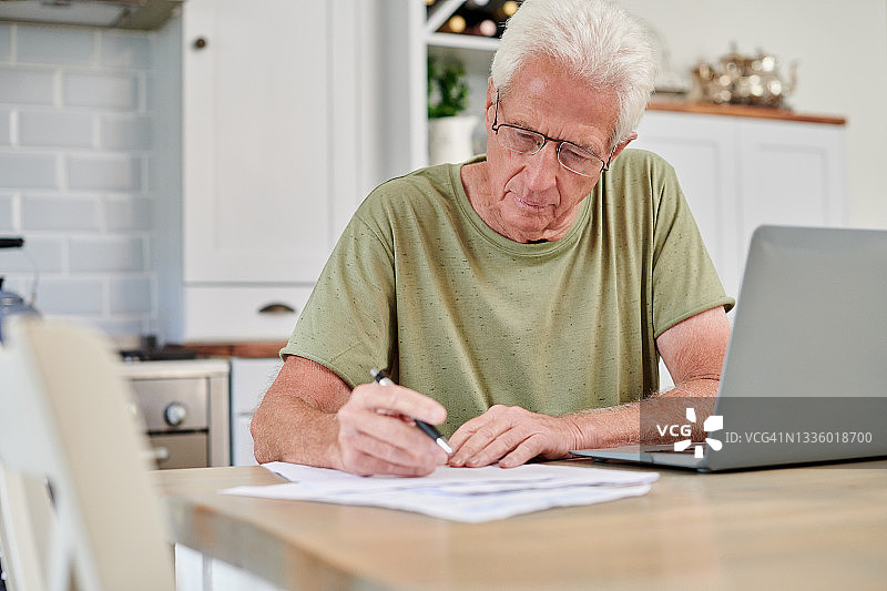 年长的男人在家中使用笔记本电脑处理文件照片图片素材