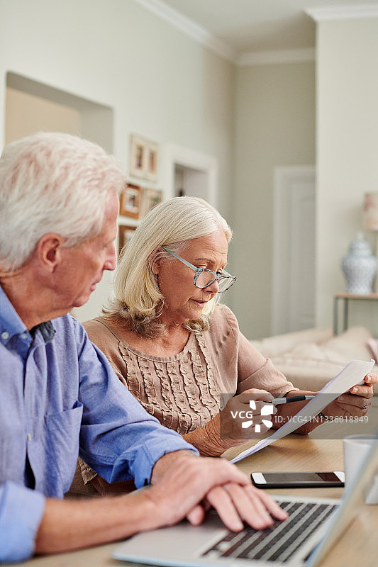 一对年长的夫妇在家中使用笔记本电脑并处理文书工作图片素材