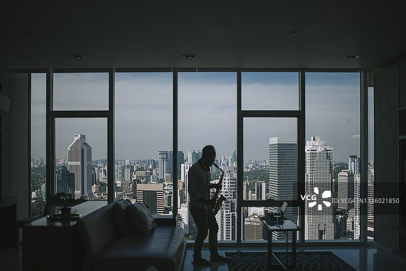 在剪影中，亚裔活跃老年男人艺术家在客厅里用笔记本电脑演奏萨克斯并展示给他的学生看图片素材