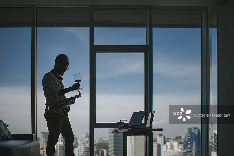轮廓生活技巧亚洲活跃老年男子艺术家喝威士忌，与朋友一起演奏萨克斯管，在客厅里使用笔记本电脑进行视频通话图片素材