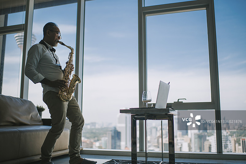 亚洲老年艺术家在客厅直播，用笔记本电脑向学生展示萨克斯图片素材