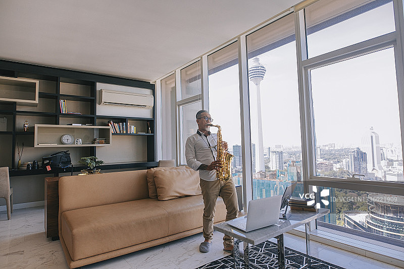 亚洲老年男艺术家在公寓客厅用笔记本电脑向学生展示萨克斯图片素材