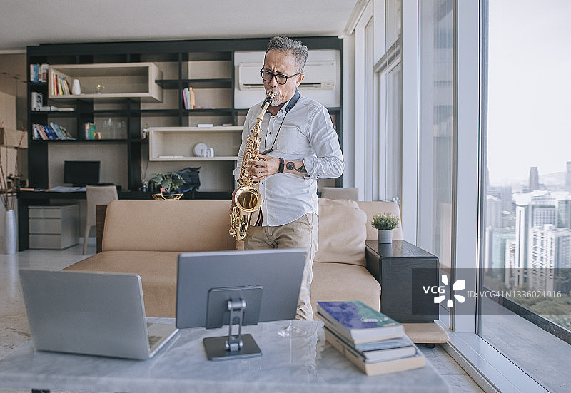 中国老年艺术家在公寓客厅通过笔记本电脑直播教学生演奏萨克斯图片素材