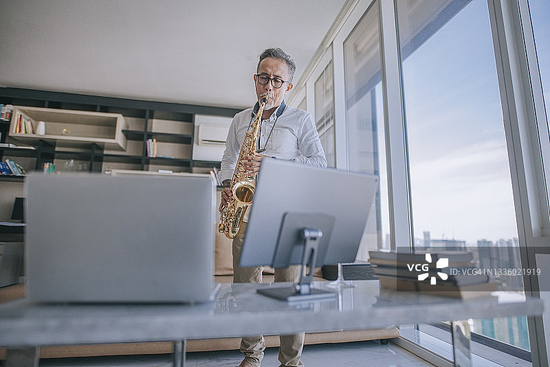 中国老年艺术家在公寓客厅通过笔记本电脑直播教学生演奏萨克斯图片素材