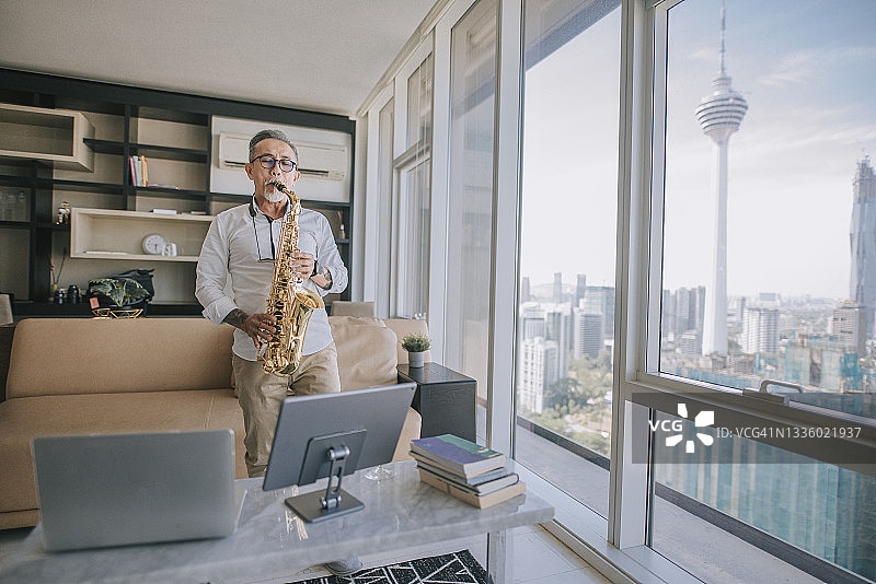 在吉隆坡城市公寓客厅，老年艺术家用萨克斯给学生上网课图片素材