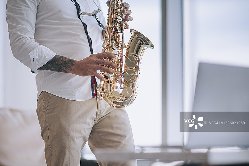亚洲男士在公寓客厅用笔记本电脑直播教学生吹萨克斯管（半身）图片素材