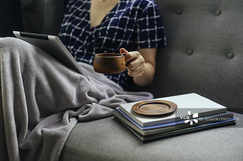 年轻成年女性坐在舒适的沙发床上，在家放松地端着木杯咖啡图片素材