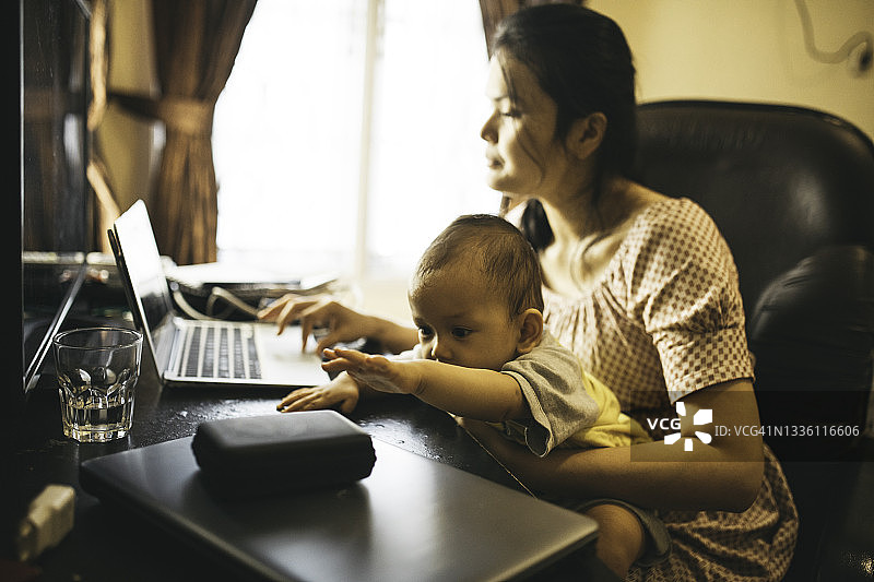 母亲在家工作时抱着婴儿图片素材