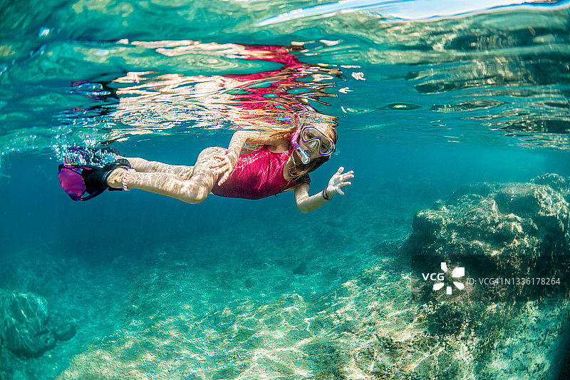 穿着粉色泳衣，戴着紫色面罩、呼吸管和脚蹼的可爱小女孩图片素材
