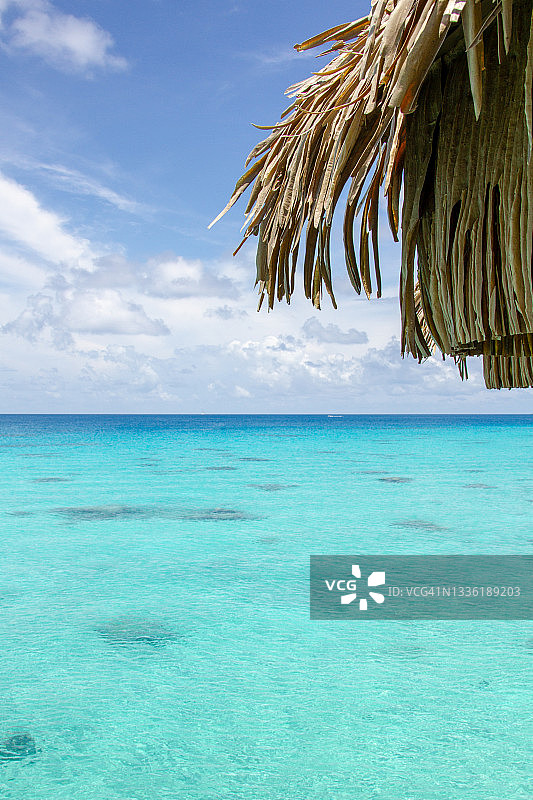 茅草屋顶一角：清晰的碧绿海水和多云的天空图片素材