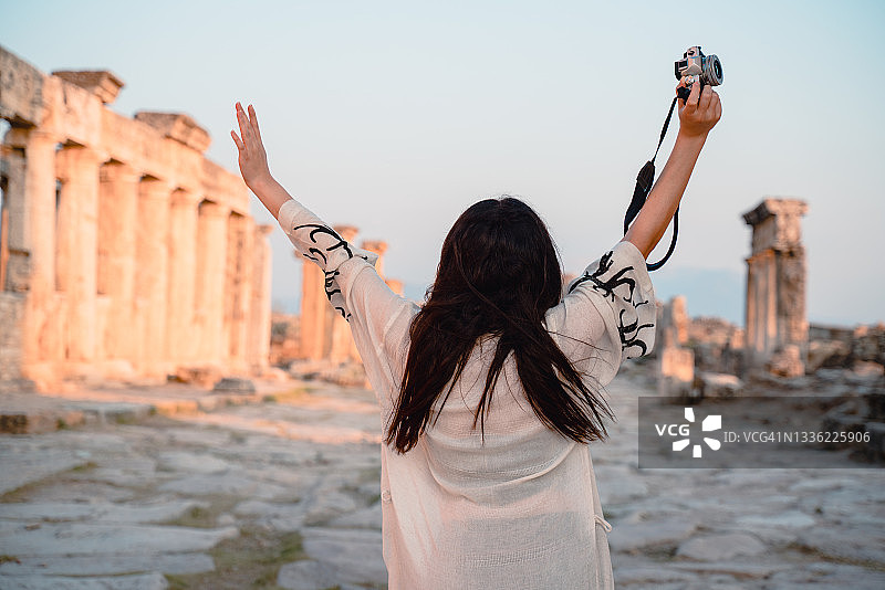 在希拉波利斯, 帕穆克卡莱古城遗址Frontinus门前举起双臂的女游客图片素材