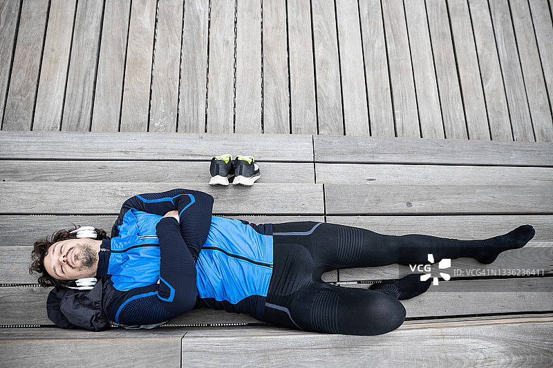 年轻运动员戴着耳机躺在木板路台阶上闭目休息图片素材