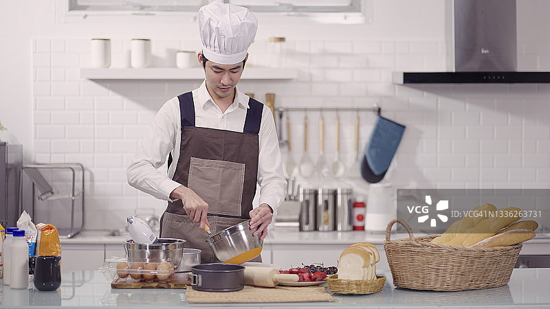 年轻男厨师在厨房用搅拌器搅拌面糊图片素材