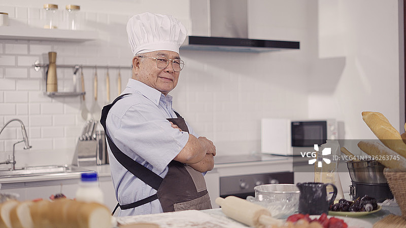 在厨房里戴着厨师帽和围裙的年长男人肖像图片素材