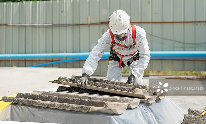 安全是我们的首要任务。工人身穿全身防护服，正在处理石棉屋顶瓦片。图片素材