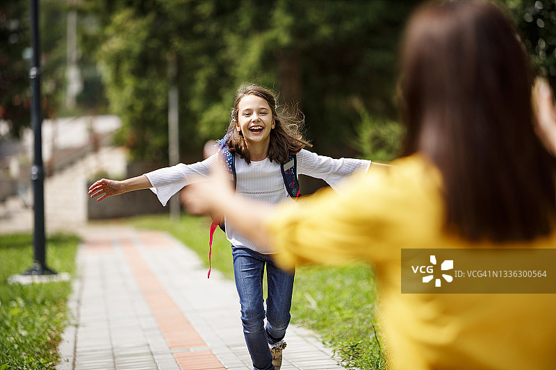 快乐的女学生放学后跑去拥抱母亲图片素材