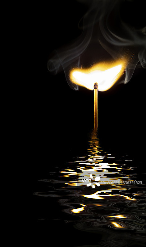 黑色背景上火柴的火焰和烟雾在水面上的倒影图片素材