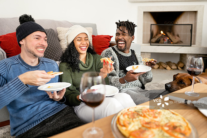 在冬天，朋友们在家里的炉火旁吃披萨和喝红酒，欢声笑语图片素材