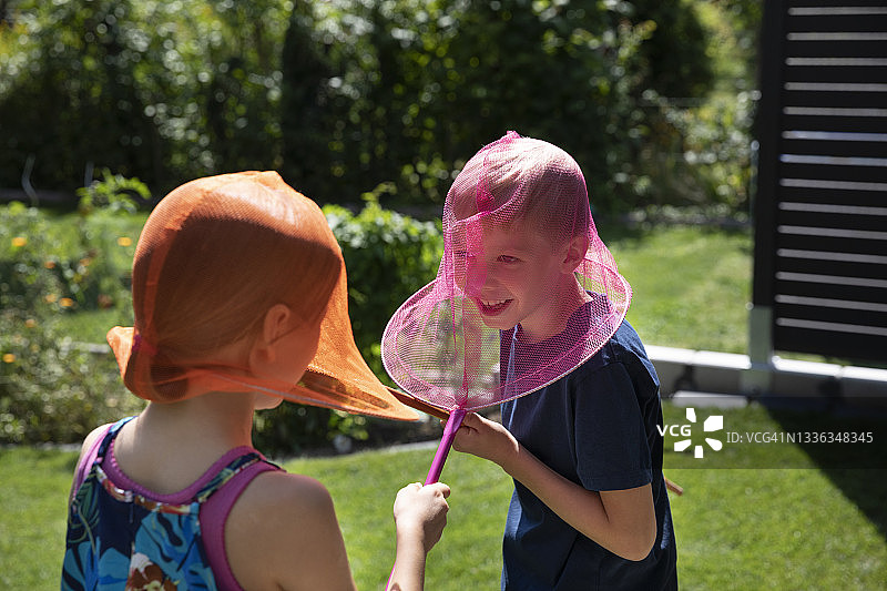 两个孩子在夏日后院用彩色蝴蝶网互相追逐图片素材