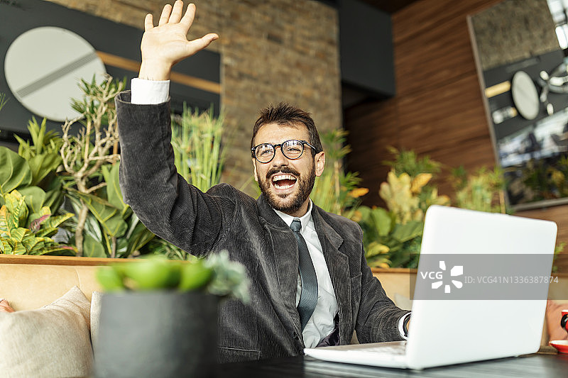 穿商务套装的年轻男人坐在咖啡馆里发送问候图片素材