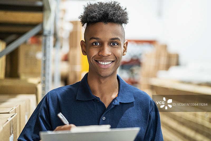 站在可持续仓库内纸箱旁边的微笑青年图片素材