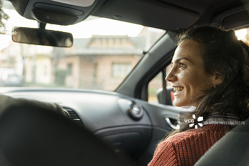 坐在车内乘客座位上的微笑的年轻女子侧视图图片素材