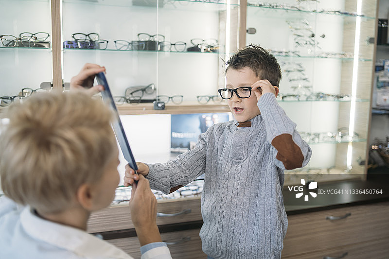 眼科医生帮忙拿着镜子，男孩试戴不同的镜框图片素材