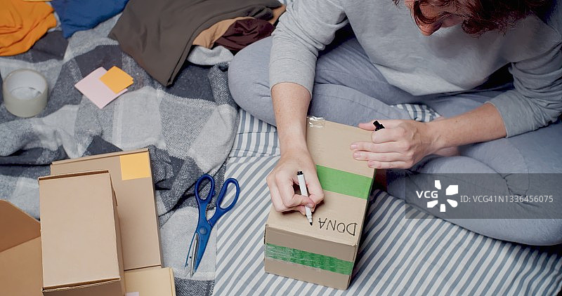 女人坐在床上整理衣物，准备捐赠图片素材