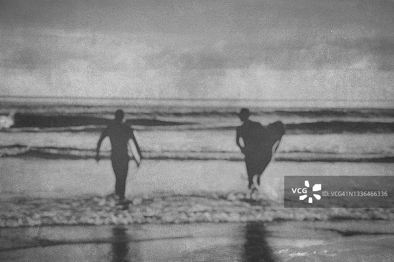 冲浪者携带冲浪板进入大海的轮廓（复古滤镜效果，模糊编辑）图片素材