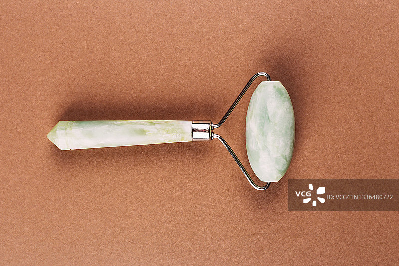 棕色背景上的面部针灸按摩用玉石滚轮工具图片素材