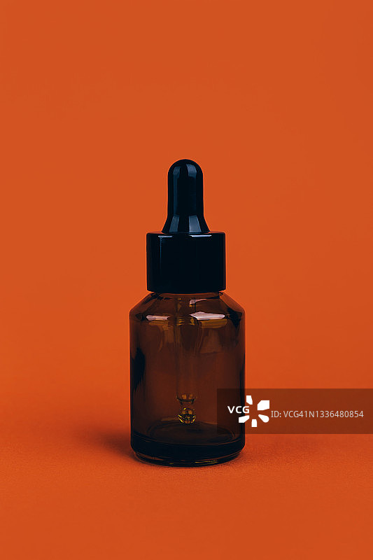 亮橙色背景上的带滴管的深绿色罐子图片素材