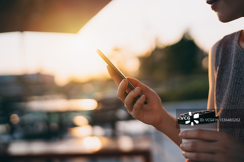 在户外长椅上喝咖啡、用智能手机的亚洲年轻女子特写图片素材