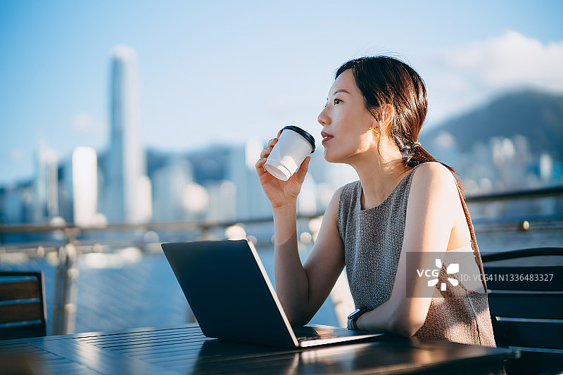 维多利亚港海滨长廊旁用笔记本电脑工作的自信年轻亚洲女商人图片素材