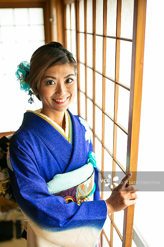 身穿和服的年轻日本女子站在传统门窗旁图片素材