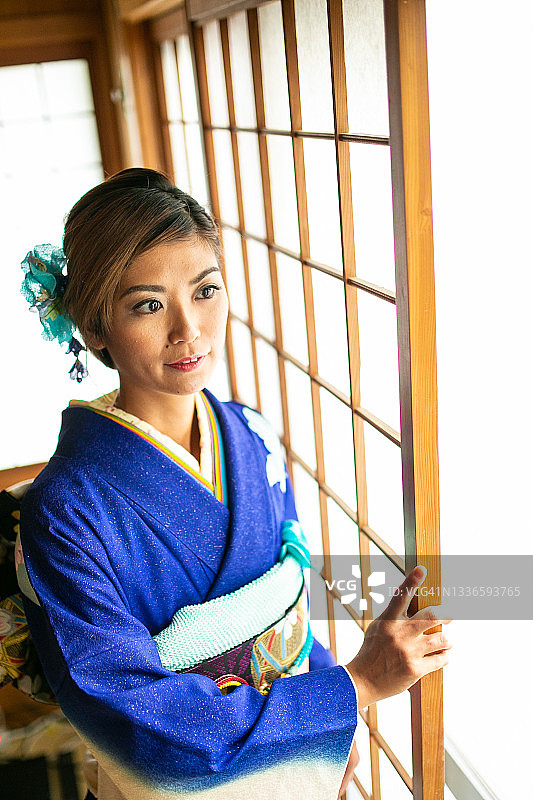身穿和服的年轻日本女子站在传统门窗旁图片素材