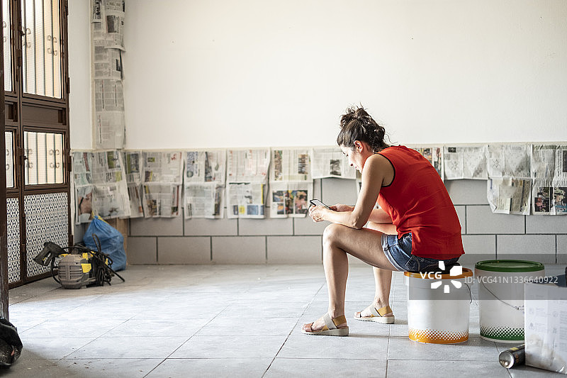 搬家和装修期间，小女孩坐在油漆桶上打字发短信图片素材