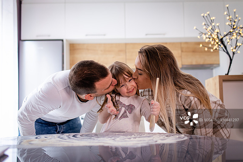 父母亲吻在厨房里制造混乱的女儿图片素材
