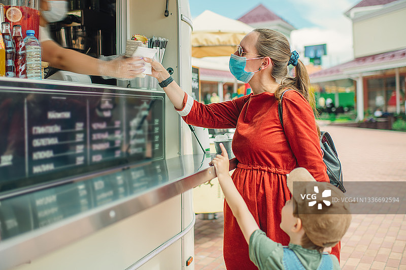 戴着防护口罩的孕妇和她的儿子在餐车购买食物和饮料图片素材