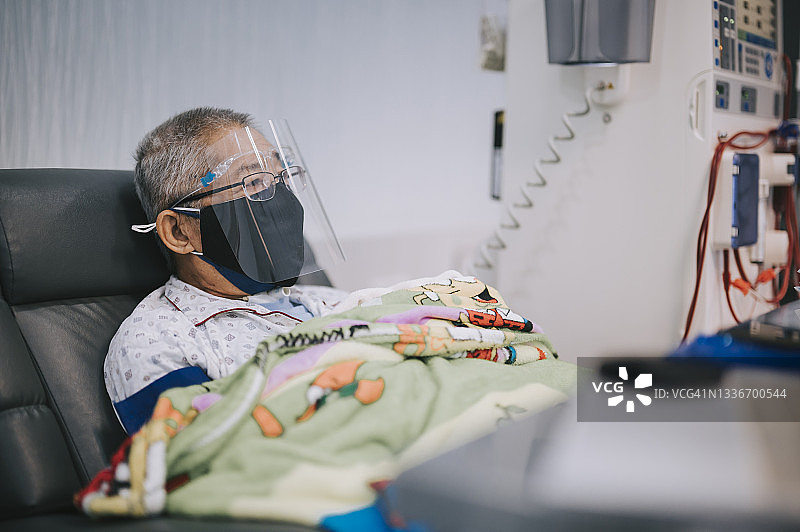 华人老年男性坐在椅子上，戴着防护面罩和口罩，在医院接受透析治疗图片素材