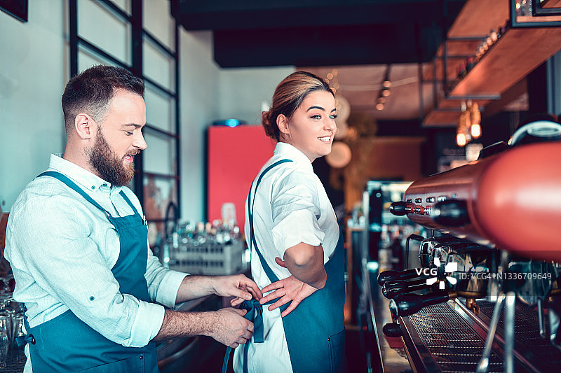 女咖啡师系上围裙，男同事帮忙图片素材