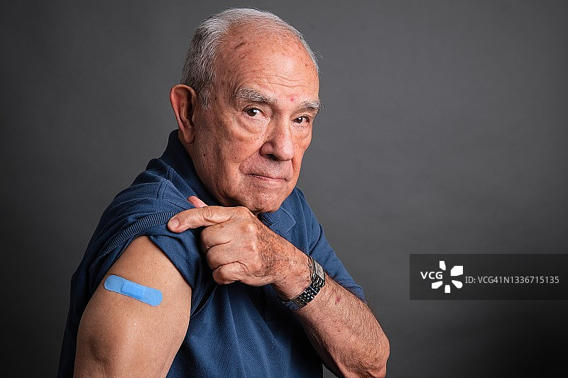 年长的男人展示手臂上的疫苗接种绷带图片素材