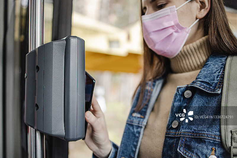 戴着防护口罩，用智能手机支付公交车票的女人图片素材
