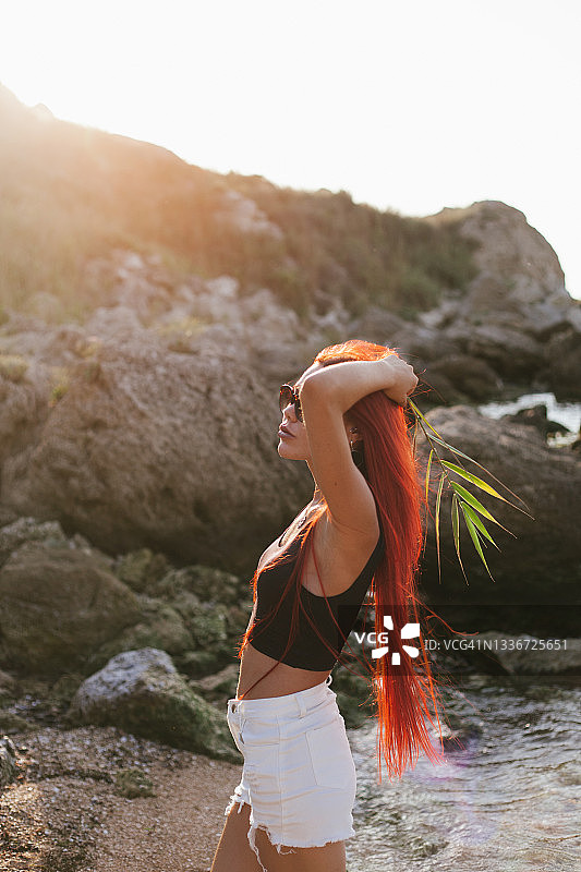在海滩享受夏日阳光的染红色长发年轻女子图片素材